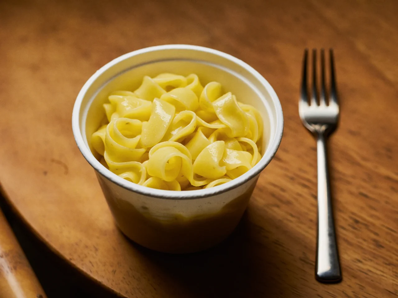 Dampfende Pasta in einem unbedruckten Behälter auf Holztisch mit Gabel