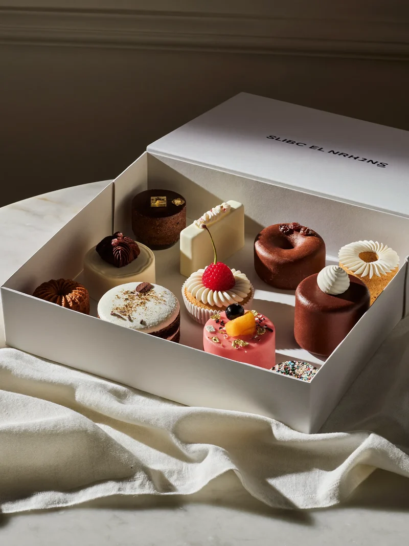 Kleine Kuchen und Gebäck in einer schlichten weißen Dessertbox auf Leinen